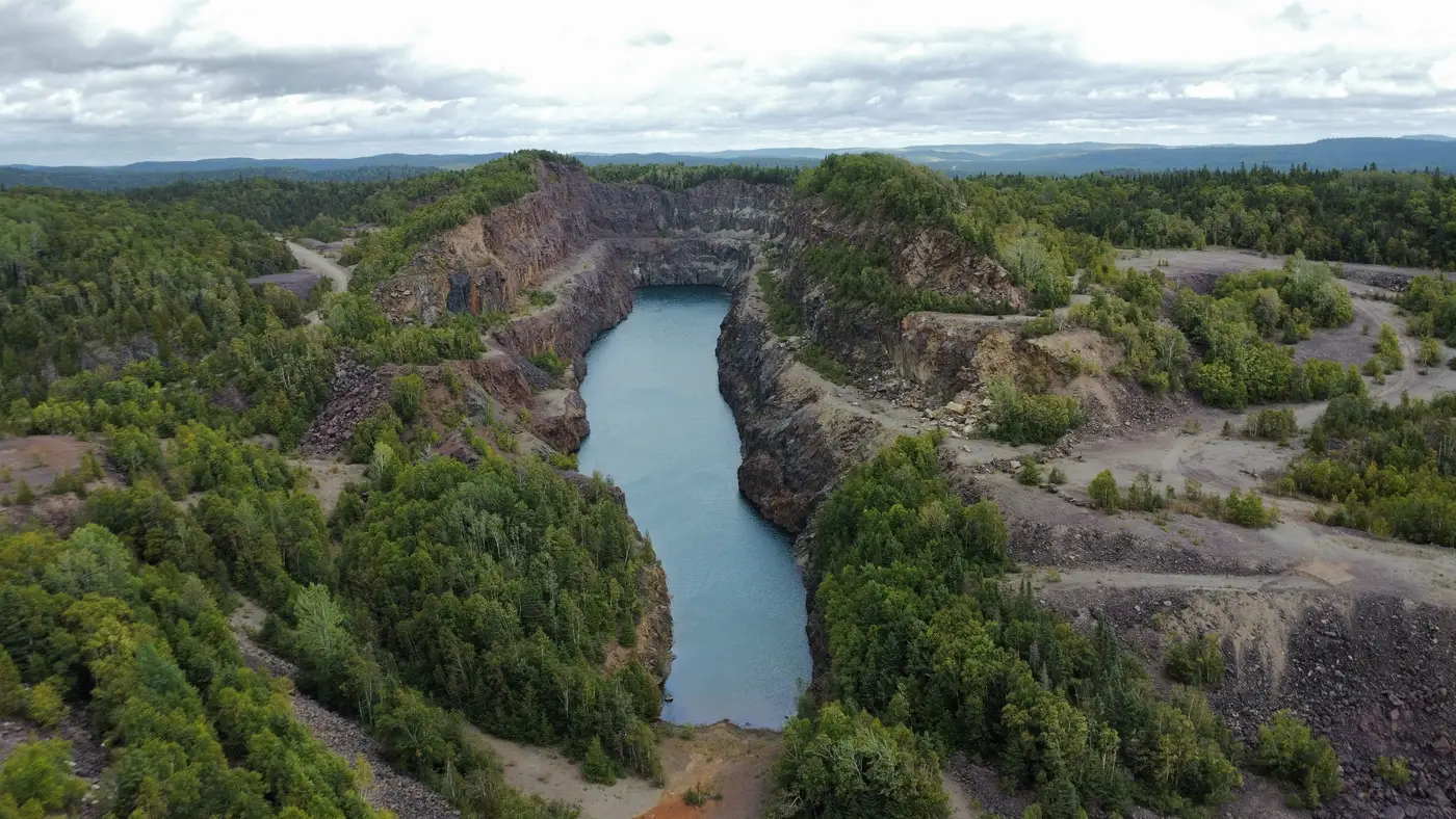 Aerial view of a water-filled pit pond held between steep rock walls, water level close under the surrounding rim.